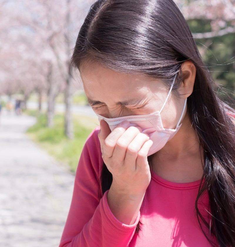 Person holding tissue near nose with allergy symptoms affecting oral health during hay fever season